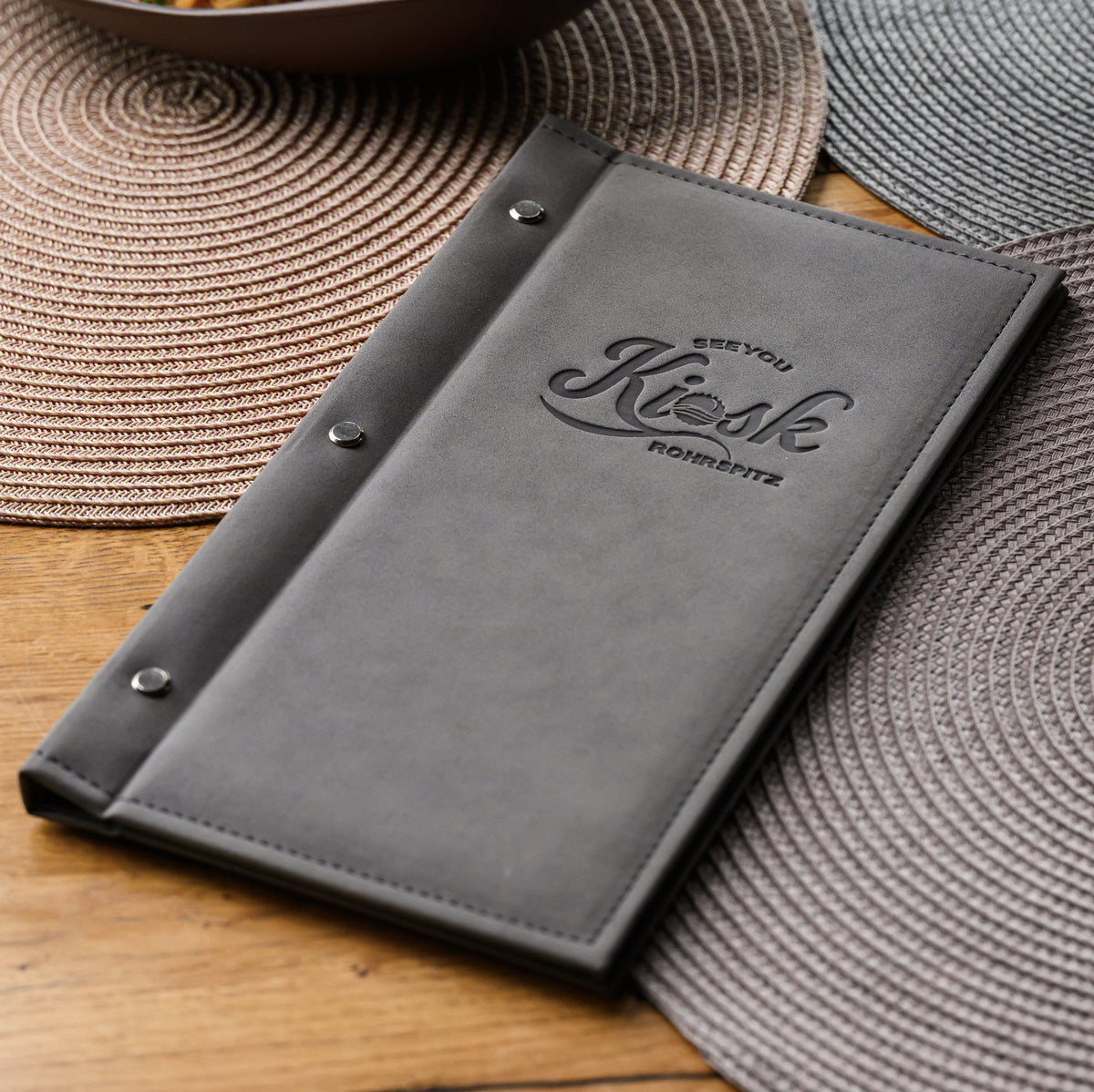 Closed nubuk hardcover menu with debossed Kiosk Rohrspitz logo and three spine screws seen from above