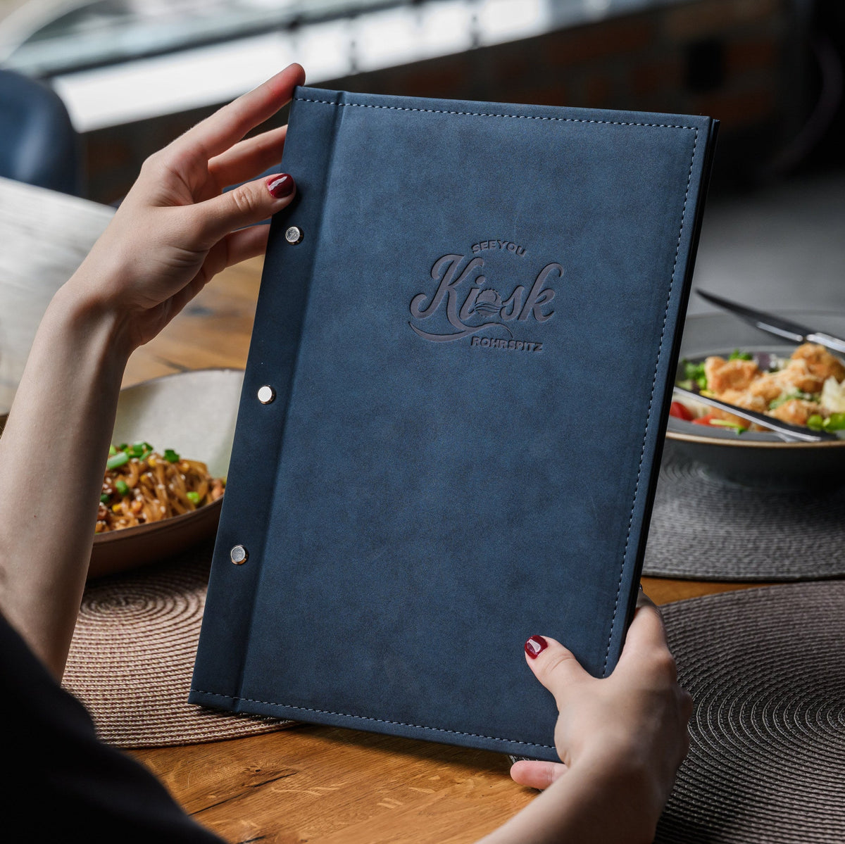 Over-shoulder view of guest opening navy nubuk menu cover with burgundy Appetizers paper insert