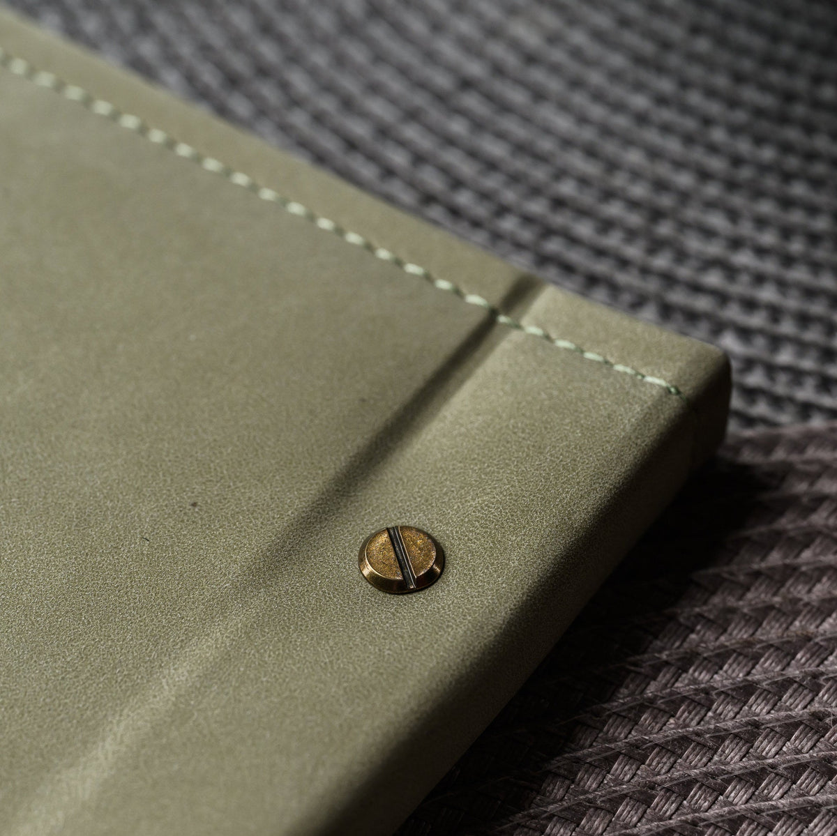 Overhead angle of olive nubuk menu cover corner with brass screw beside plated dish and placemat