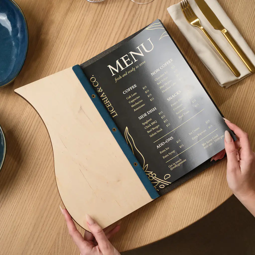 Hand opening slim plywood menu folder with denim wave panel revealing black and gold menu insert inside

