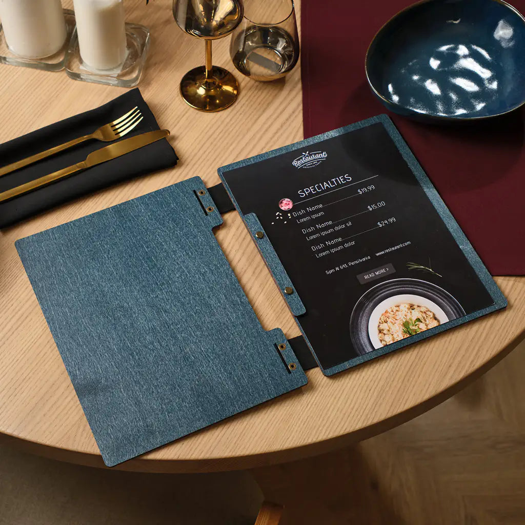 Denim blue plywood square menu folder with engraved Mria logo open on restaurant table, black food menu inside