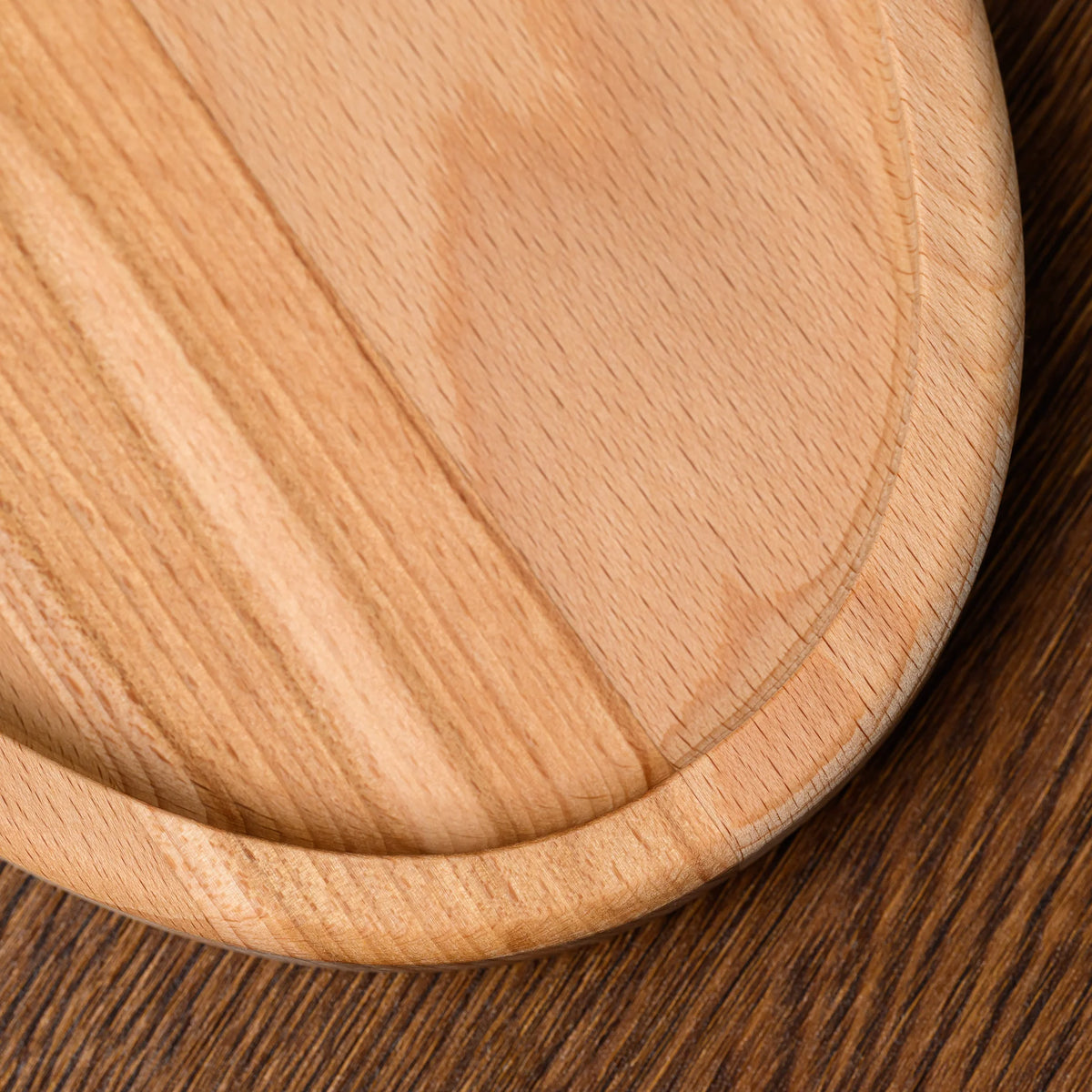Close-up of the corner and edge grain on the beech wood oval serving board, resting on a dark wooden table