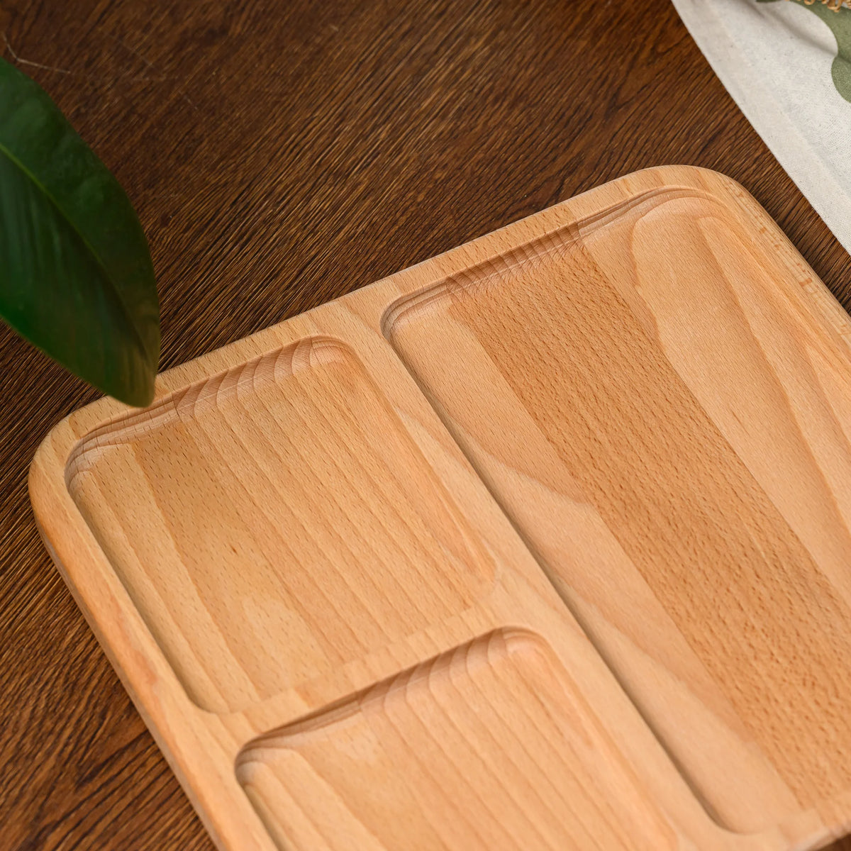 Overhead angled view of an empty beech wood serving board with three built-in compartments and rounded corners