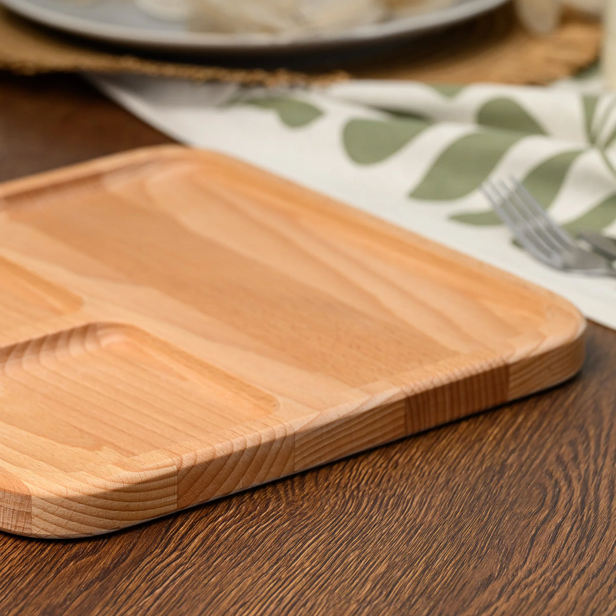 Close-up of a rounded corner and beveled edge on the beech wood serving board resting on a dark wooden table