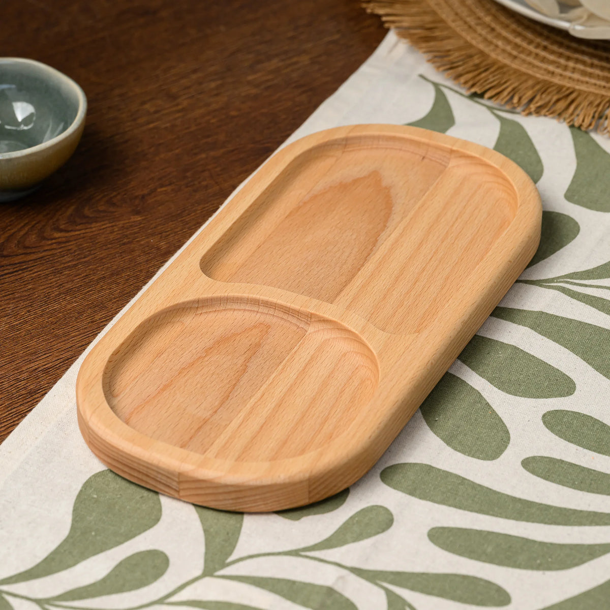 Angled view of an empty beech wood divided serving board showing both oval compartments and rounded edges