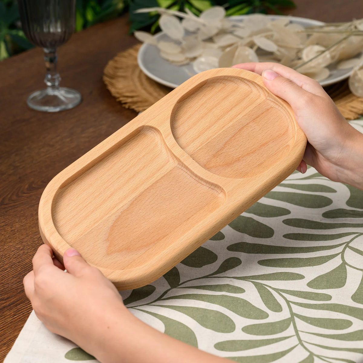 Hands holding the beech wood divided serving board at an angle above a set table with a wine glass