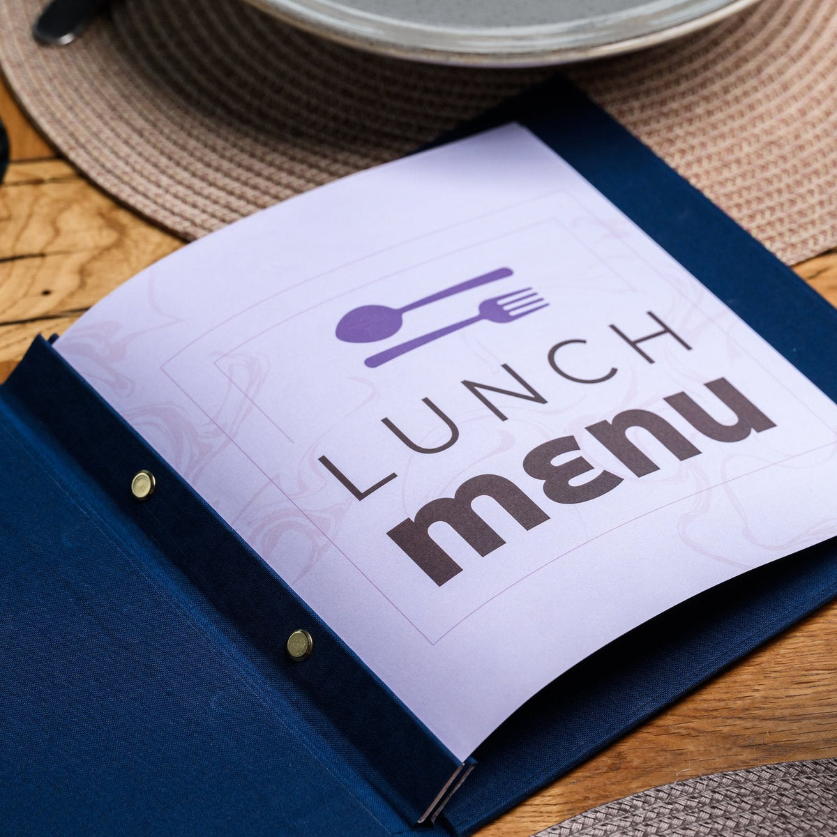 Open navy textile menu folder with a white lunch menu title page and V-notch binding on a woven placemat