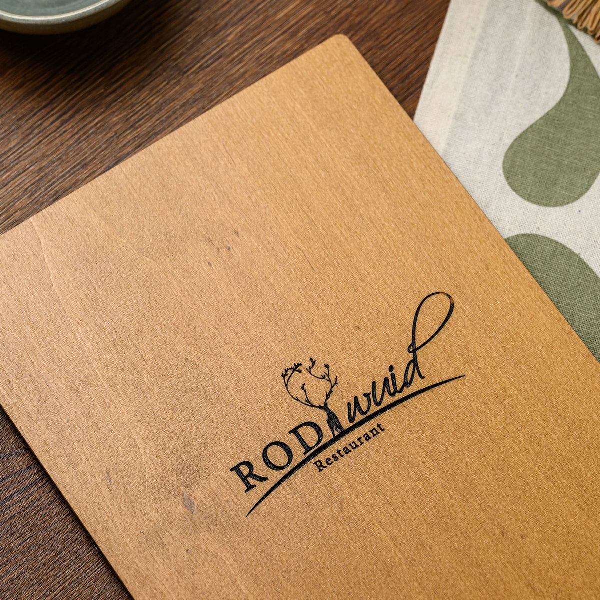 A close-up angled view of an engraved logo on the plywood back panel of this felt-front menu clipboard 