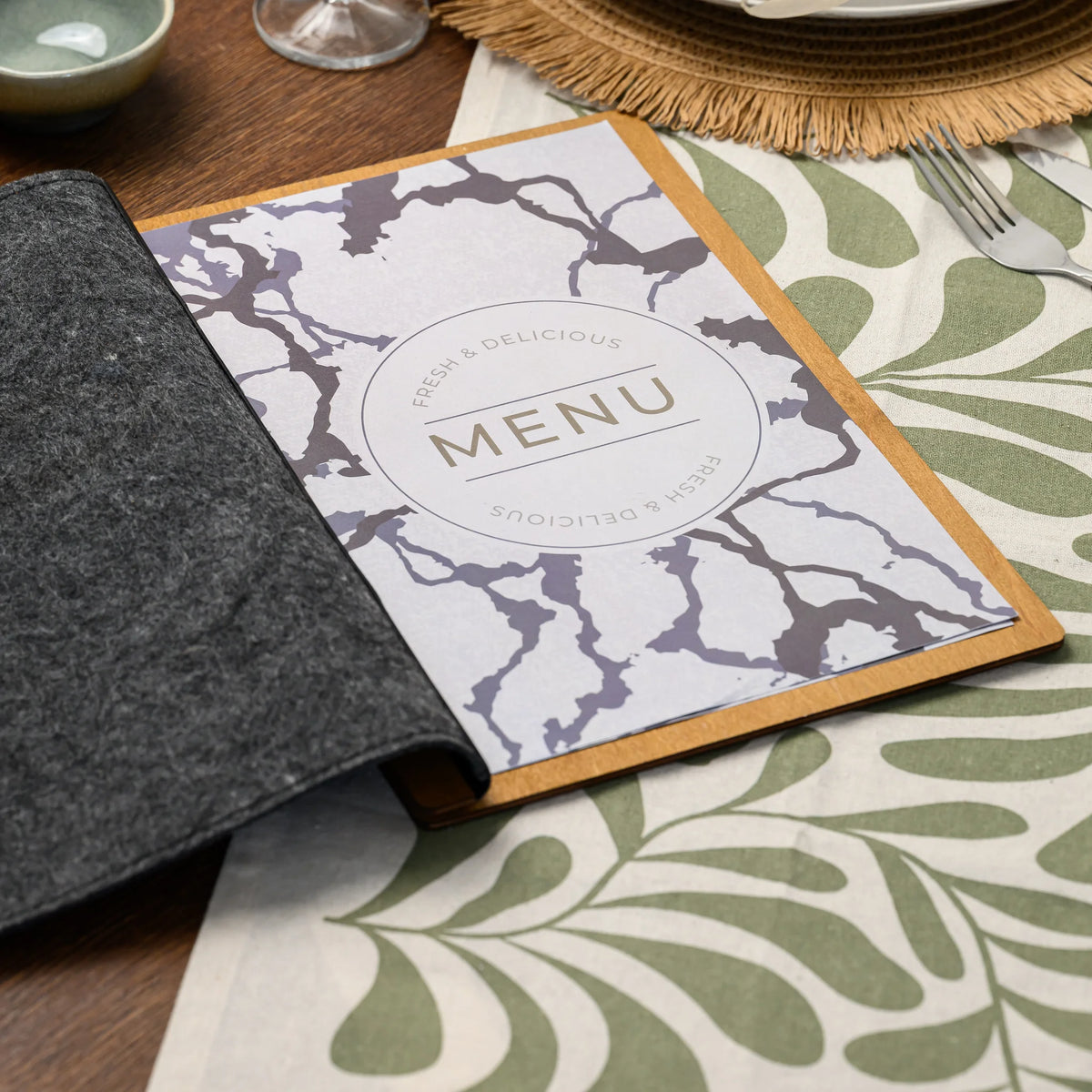 A felt-covered menu folder lying open on a restaurant table beside a ceramic bowl and a filled wine glass 