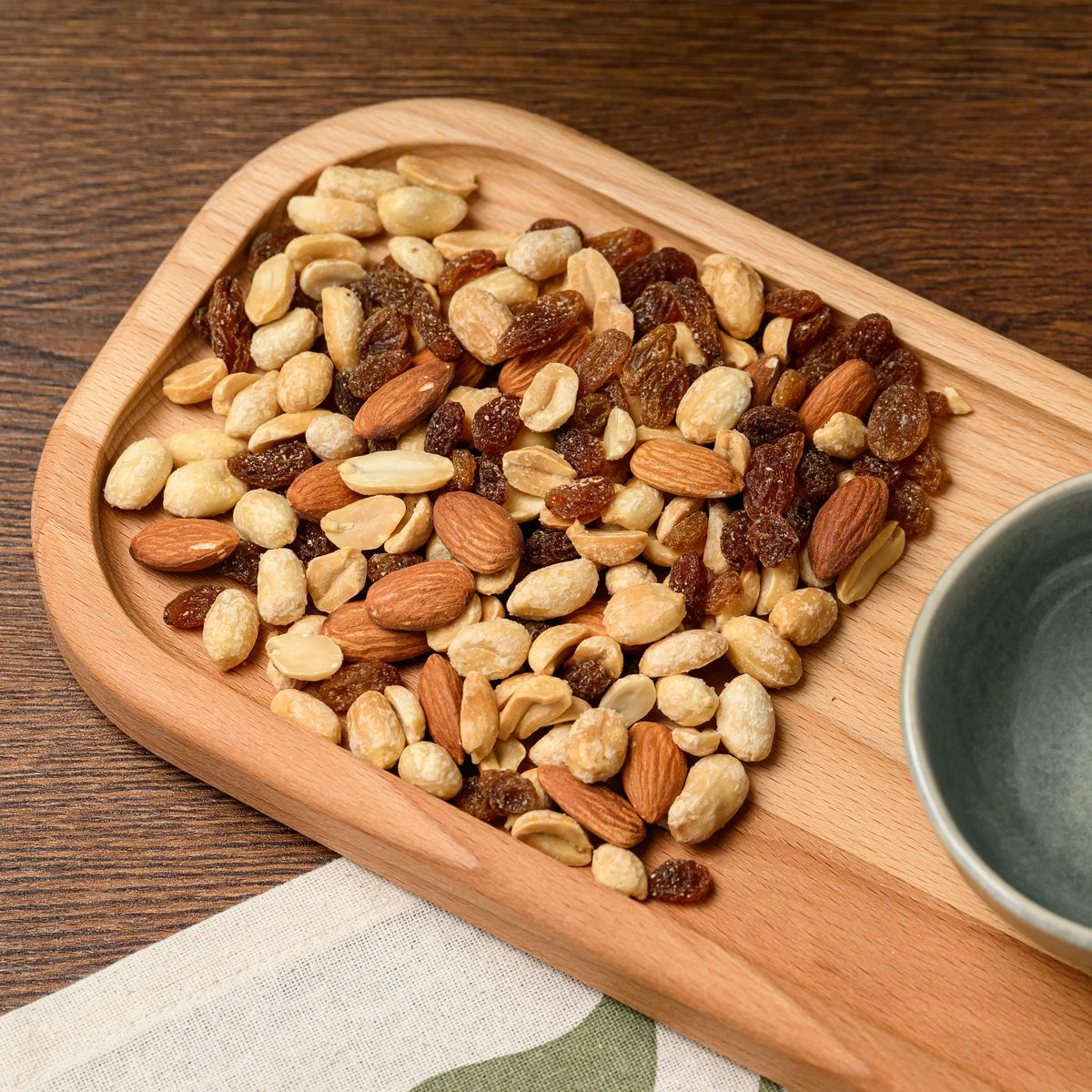 Overhead view of mixed nuts and raisins filling one end of the beech wood rectangular serving board