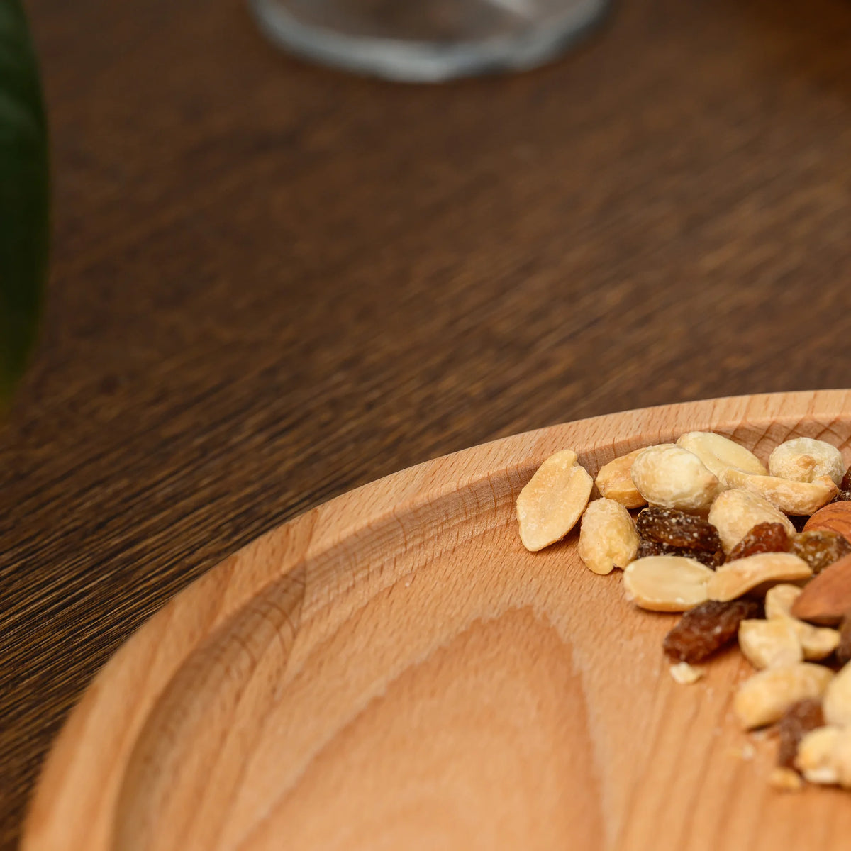 Close-up of mixed nuts and raisins spilling over the raised rim of the round beech wood serving plate