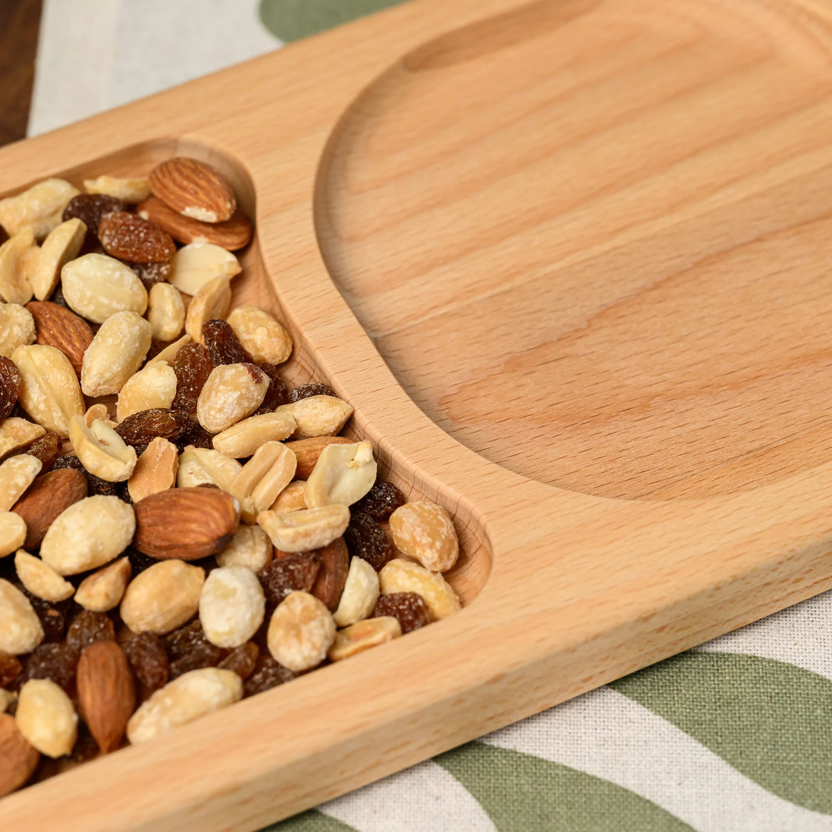 Close-up of mixed nuts filling one oval compartment next to the empty compartment on the beech wood board