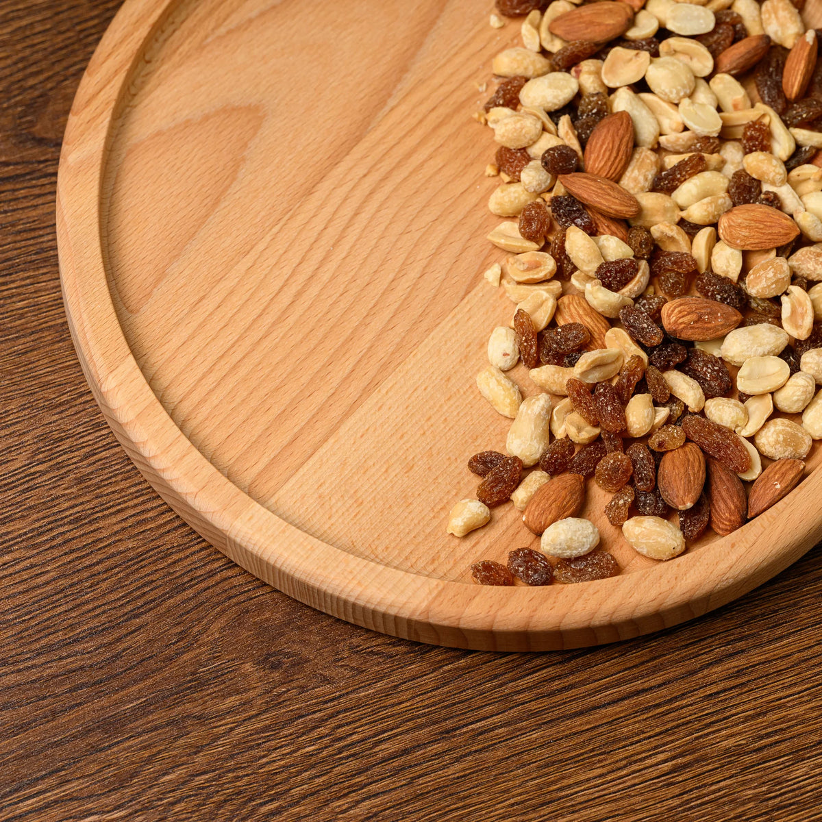 Close-up of mixed nuts and almonds filling half of the round beech wood plate, with the rim visible at the edge