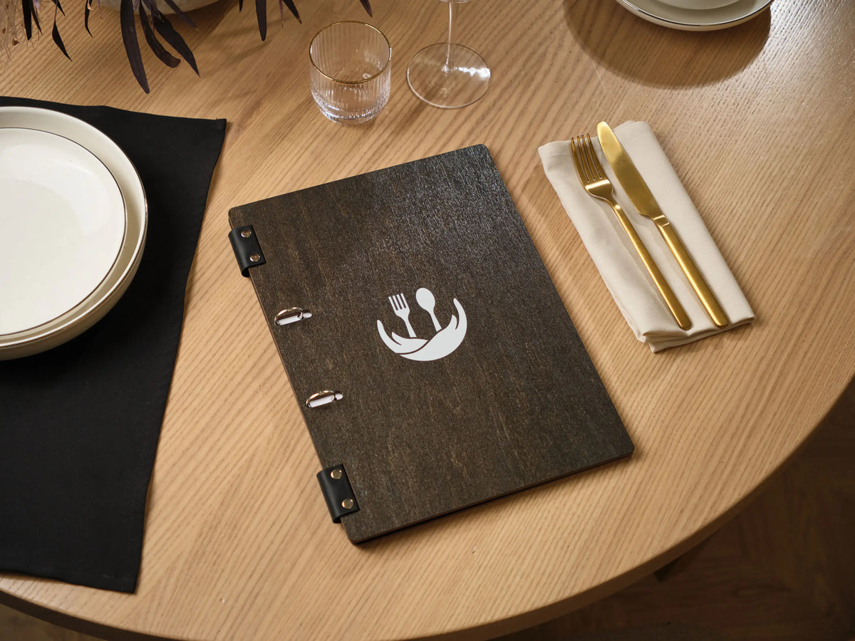 Dark wenge plywood menu folder with engraved round fork spoon logo on round wooden restaurant table
