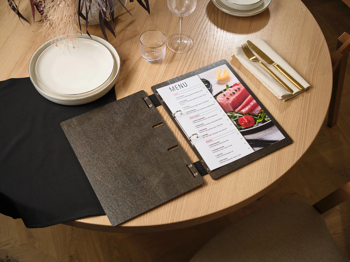 Open dark wenge plywood menu folder with white food photo menu insert on round wooden restaurant table
