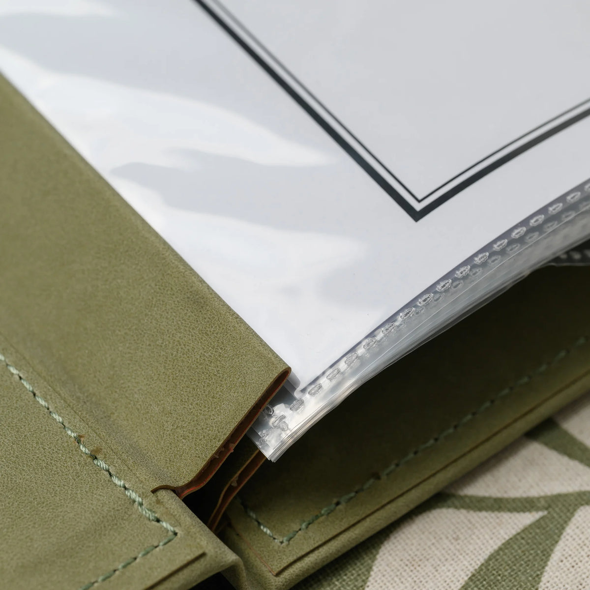 Close-up of the leather-wrapped plank of an olive menu cover holding the punched edges of clear plastic sleeves