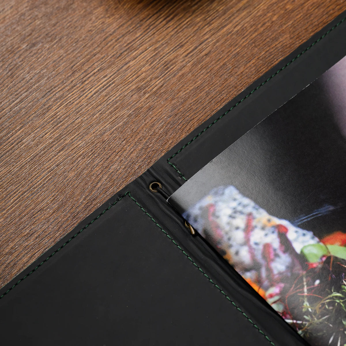 Overhead detail of black leather lining with green stitching, brass eyelet and elastic holding folded insert