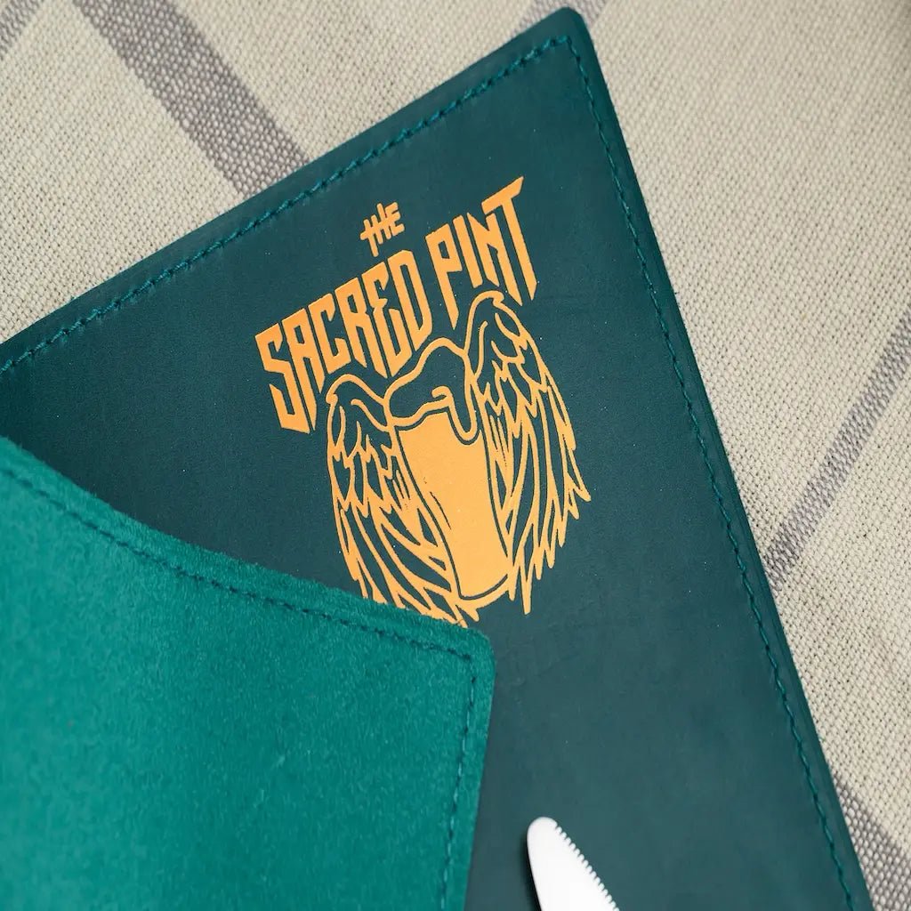 Teal mat with 'The Sacred Pint' logo featuring a winged glass on a checkered fabric background.