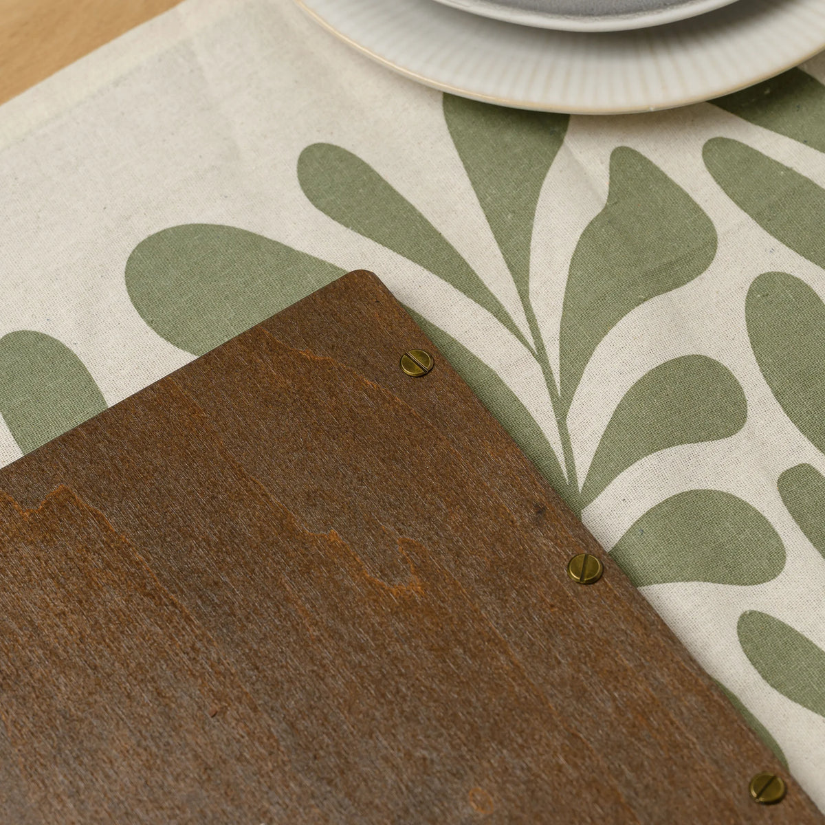 Corner of a walnut plywood menu cover back with slotted brass screws lying on a table runner next to a fork