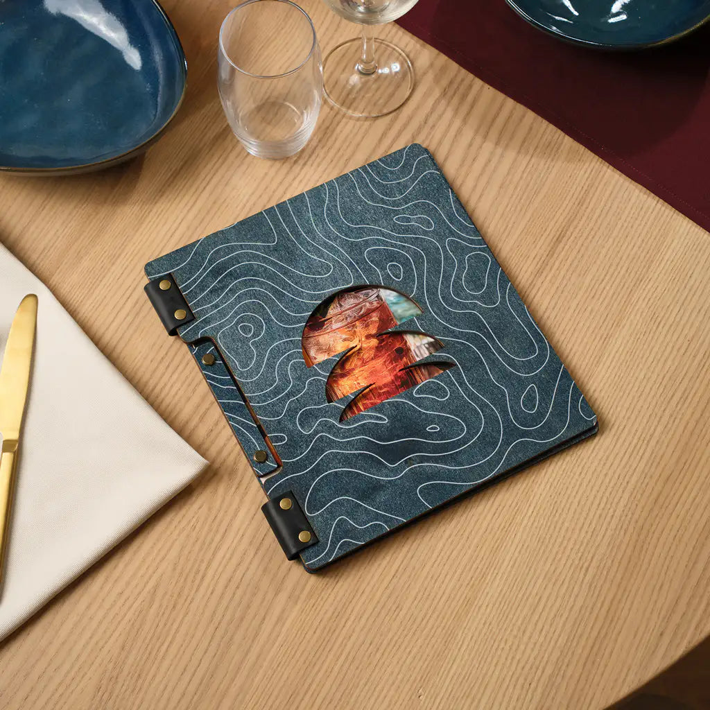 Closed denim blue plywood square menu folder with round cutout on the front cover, brass snap buttons on spine