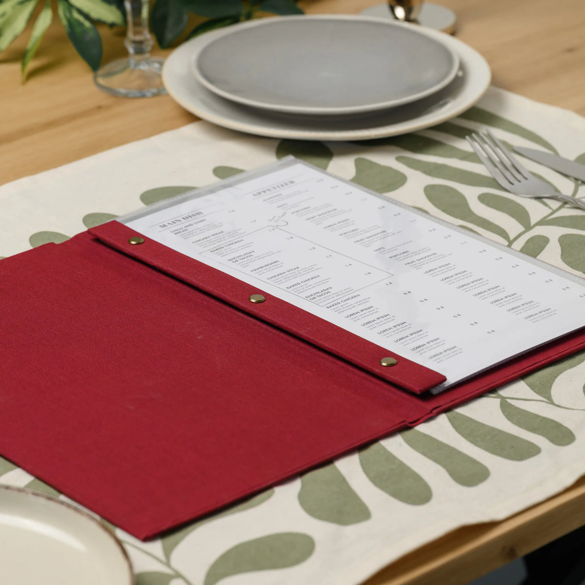Top view of an open red fabric menu cover with three brass screws on the inner plank and a menu in a plastic sleeve