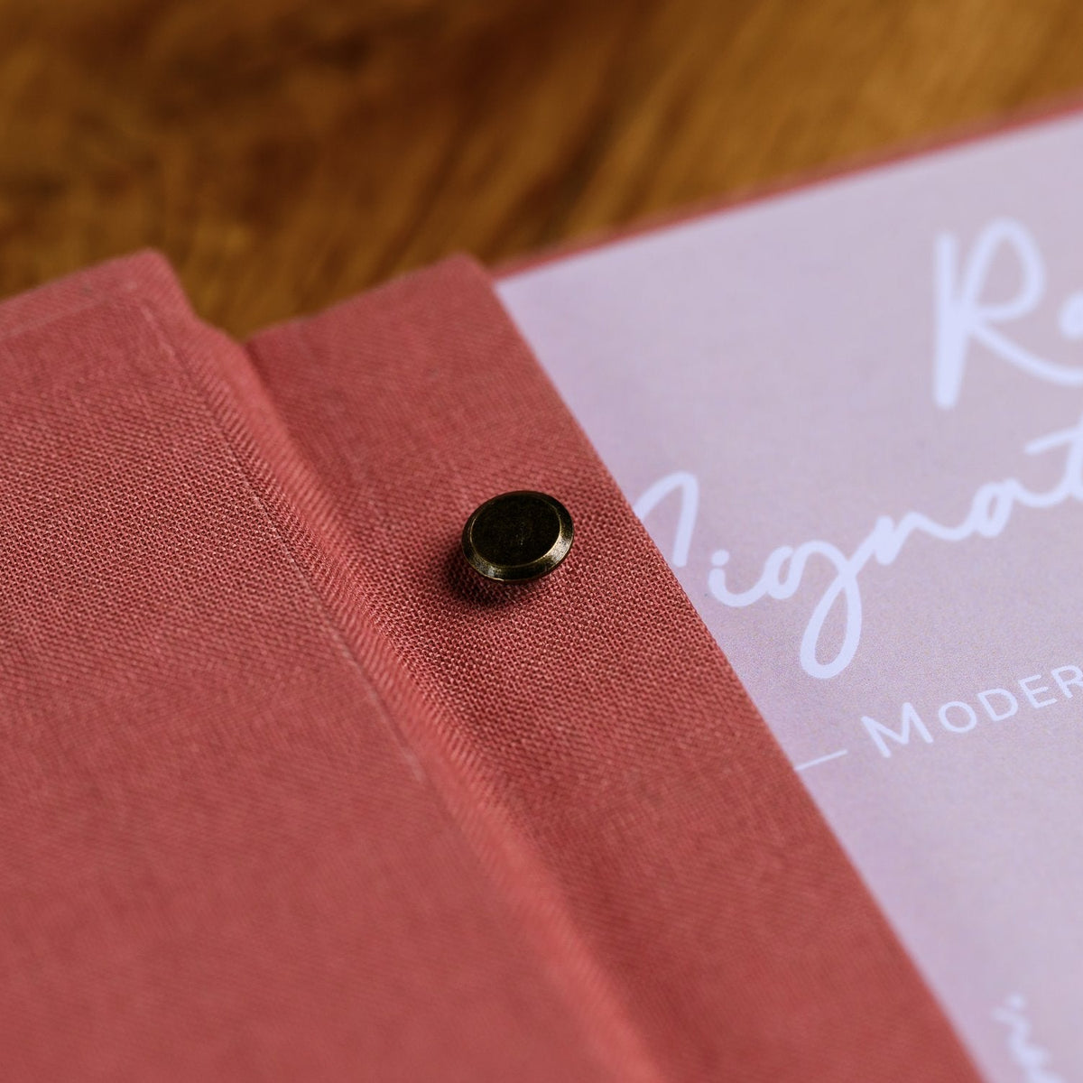 Close-up of an open coral-pink textile folder corner with a rivet fastener and a cursive text page visible