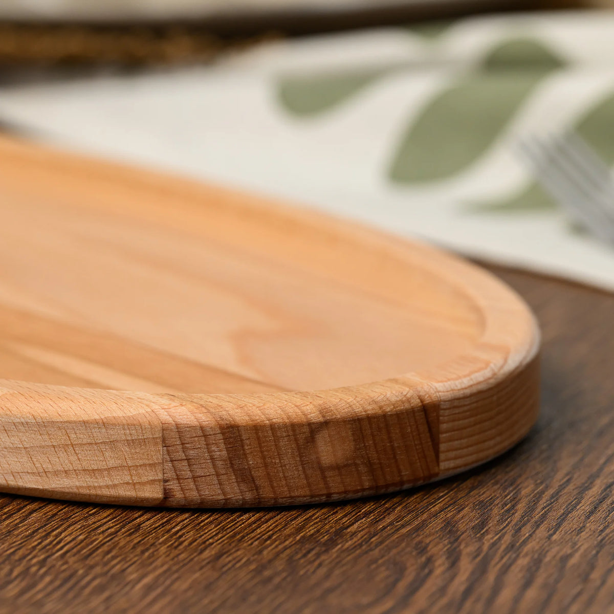 Close-up of the rounded end of the beech wood oval serving board resting on a folded linen napkin