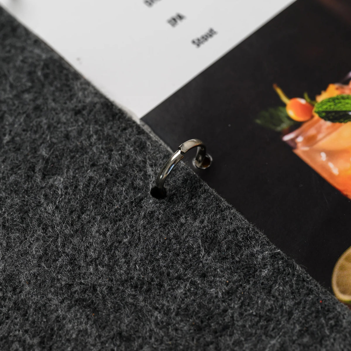 An extreme close-up of a single metal ring mechanism securing a printed menu page to the felt cover fabric 