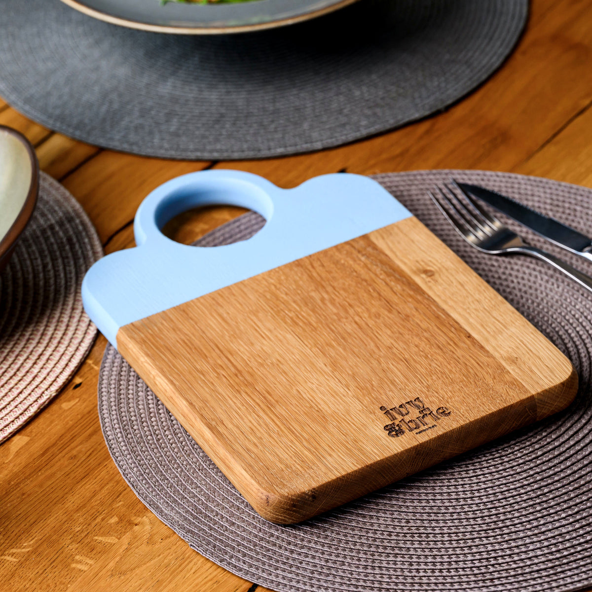 Angled view of two-tone oak snack board with light blue painted section and Ivy and Brie engraved brand mark