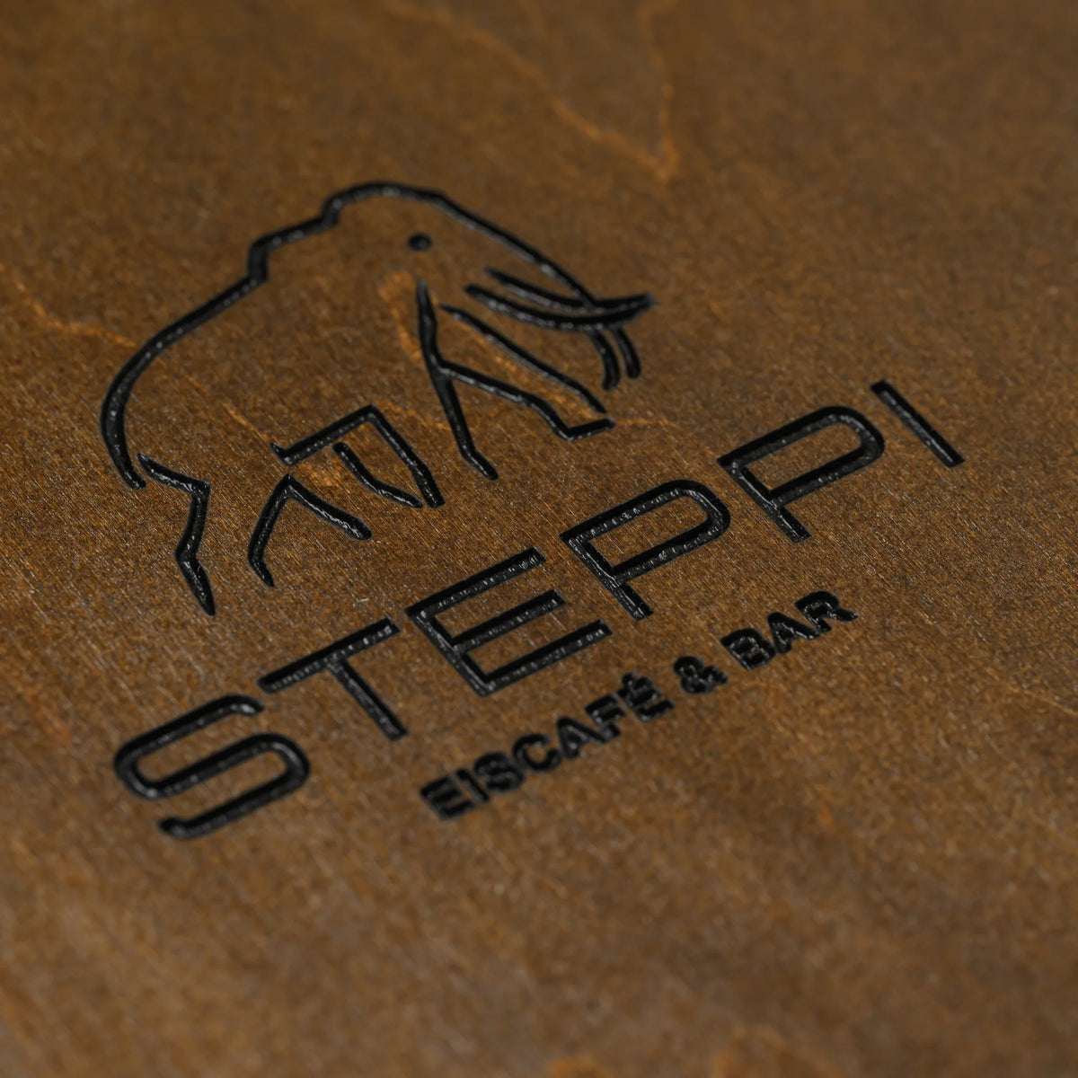 Close-up of an engraved logo with lettering on the front of a walnut plywood menu cover next to the leather strap