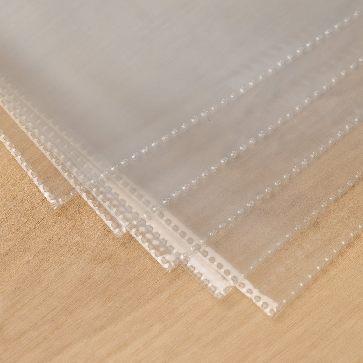 Several clear plastic menu page protectors fanned out on a wooden table, showing the dotted seams on every sleeve