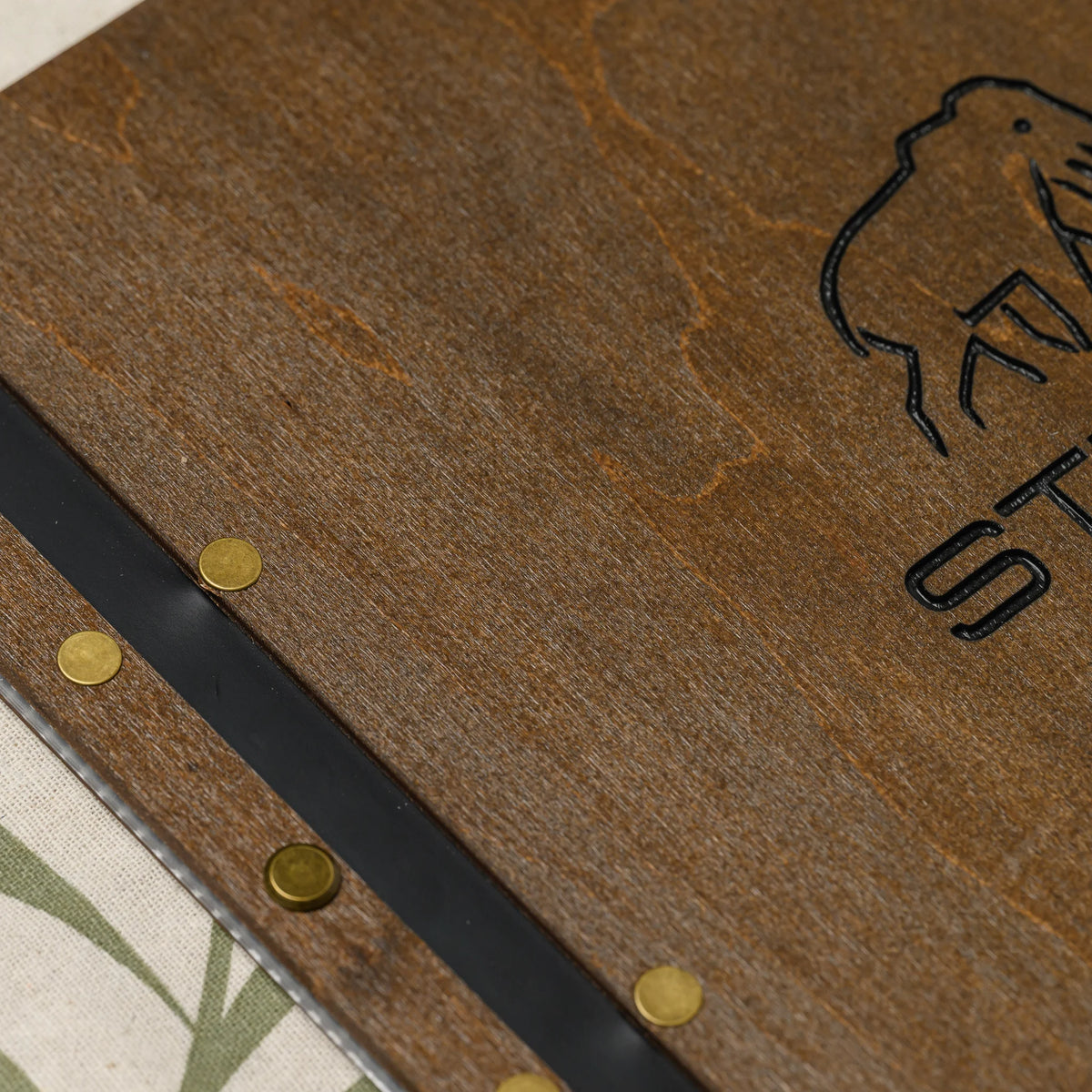 Inner leather strap of a wooden menu cover with a brass eyelet holding the punched edges of clear plastic sleeves