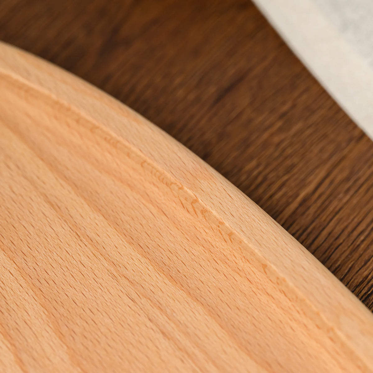 Angled view of an empty beech wood oval serving board resting on a leaf-patterned linen tablecloth