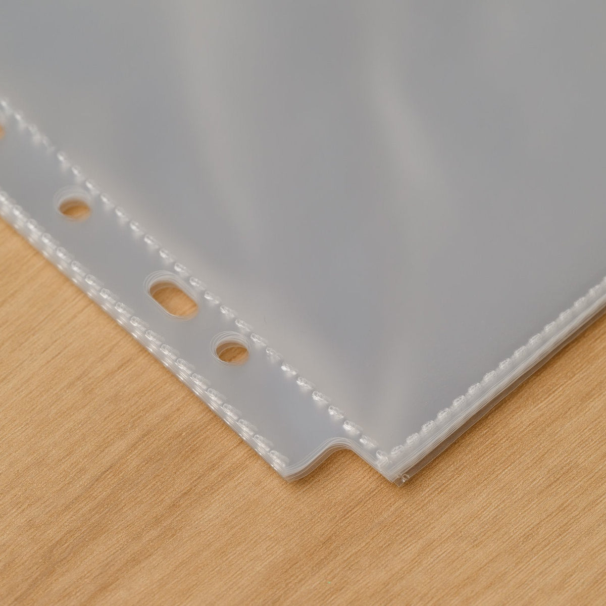 Close-up of a hole-punched menu sleeve corner with round and oval binding holes and a sealed seam on the edge