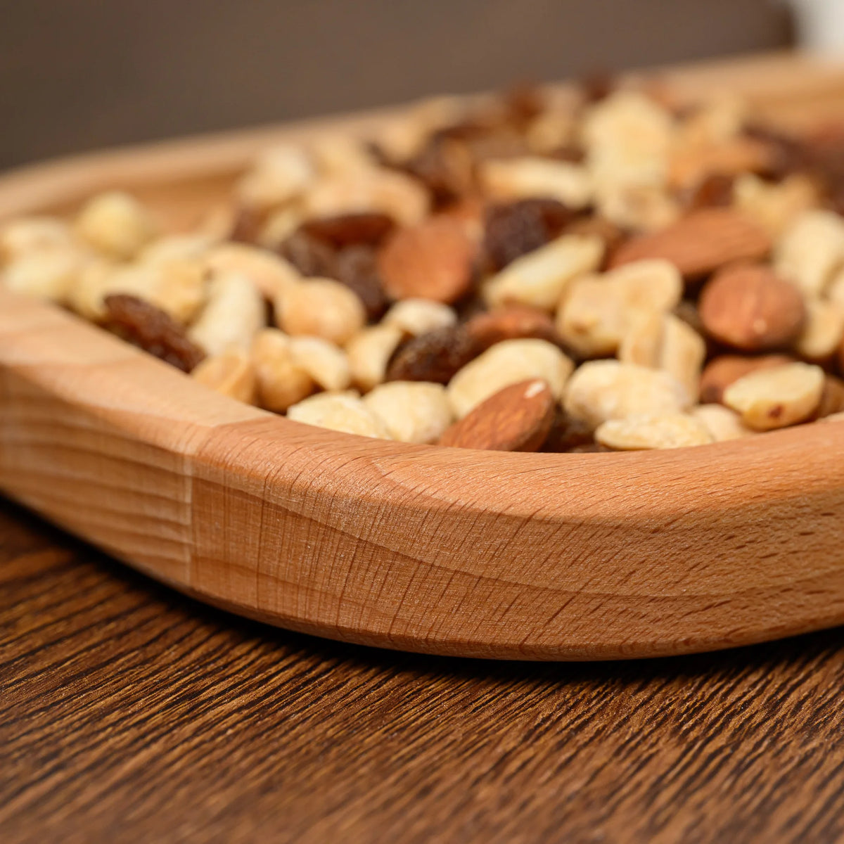 Close-up of the rounded corner and raised rim of the beech wood board, filled with mixed nuts and raisins