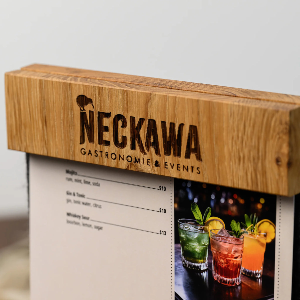 A close-up of an engraved oak bar clamped onto a felt panel, holding a printed drinks menu page in place