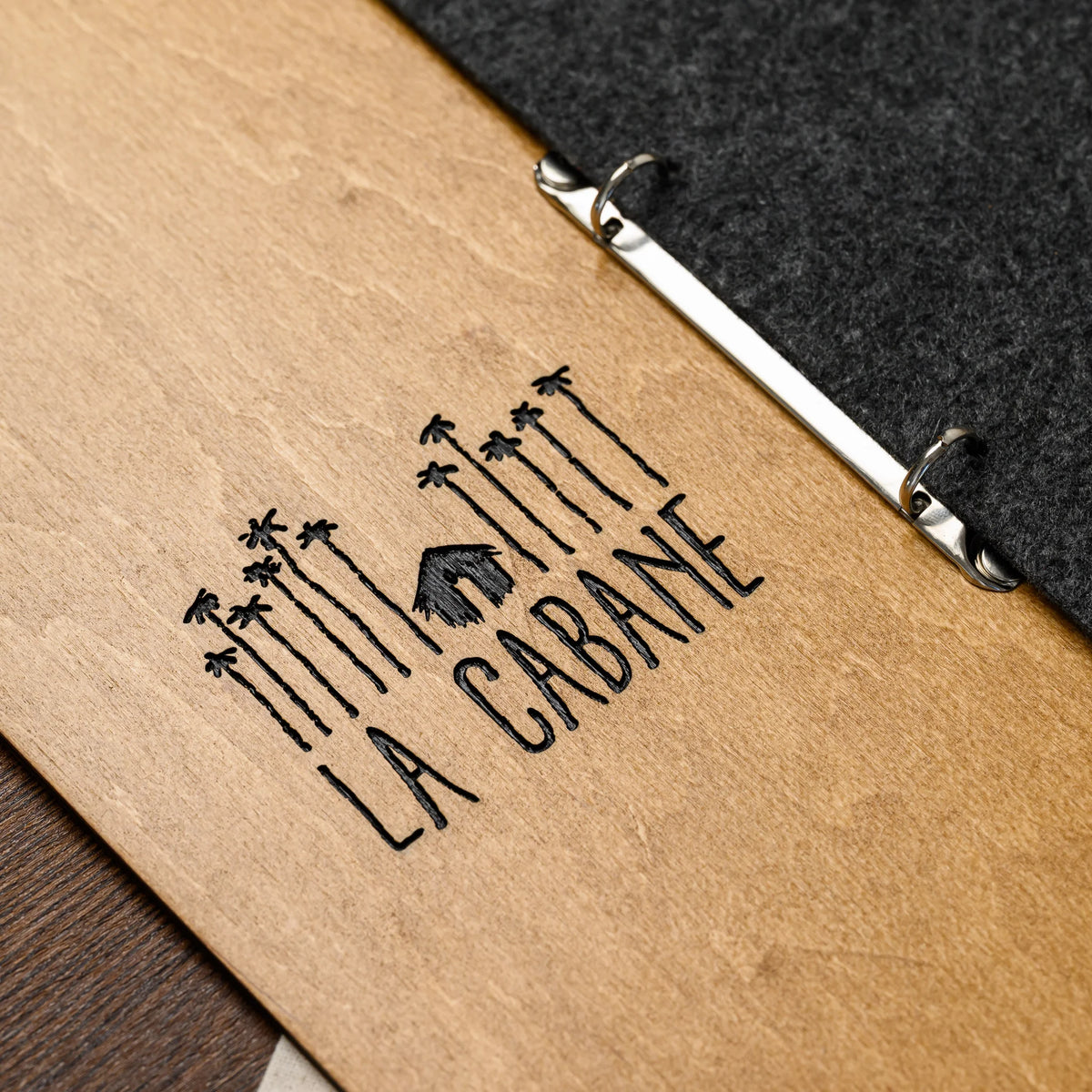 A macro view of an engraved logo detail on the plywood front, with the metal rings and felt edge visible 
