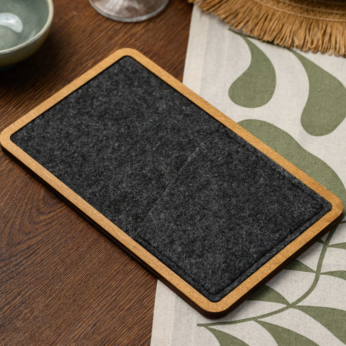 A wood-framed bill presenter with a charcoal felt pocket lying flat on a set restaurant table nearby 