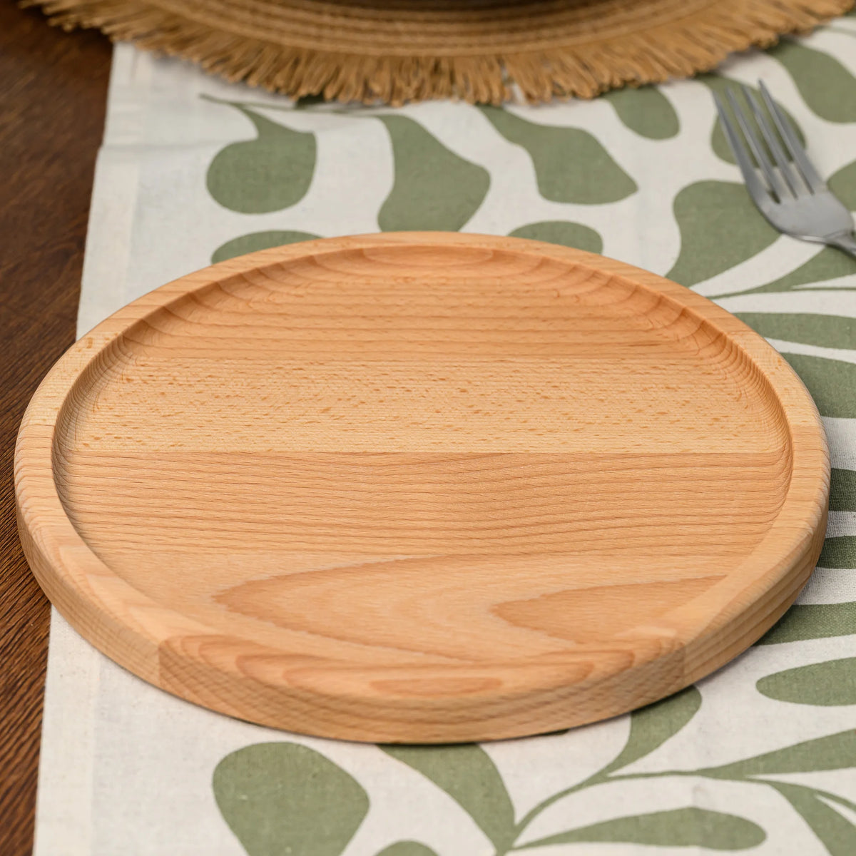 Overhead angled view of an empty round beech wood serving plate placed beside a fork on the tablecloth