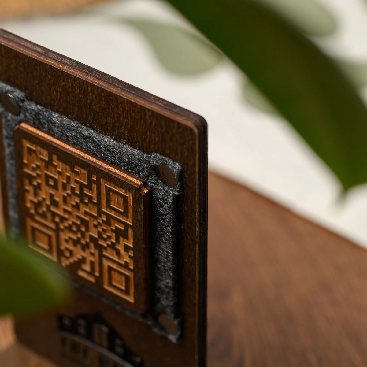 Side profile view of a wooden QR code table stand showing the felt frame edge and engraved logo detail