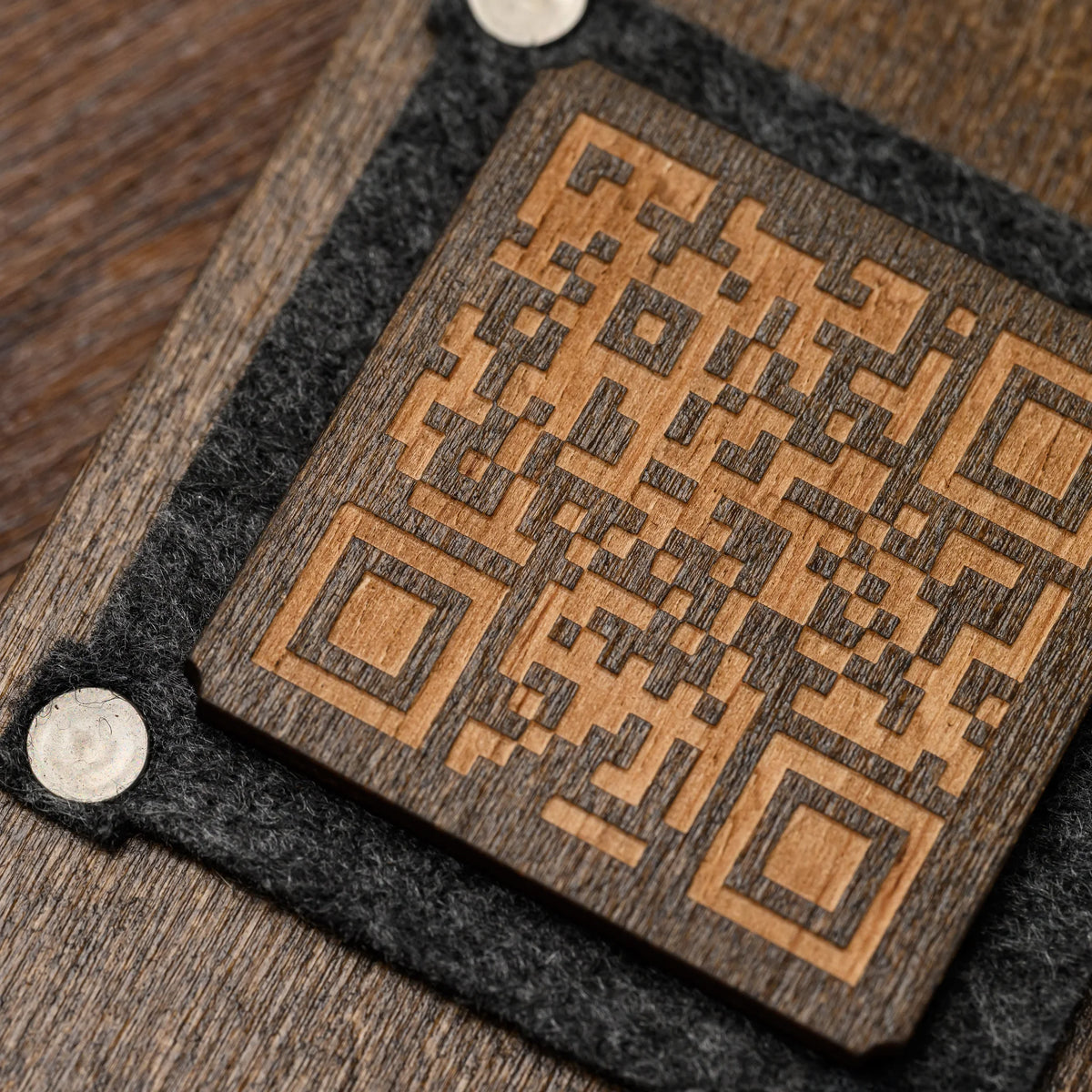 A macro close-up of a felt frame corner rivet and an engraved QR code wood panel on the table stand surface 