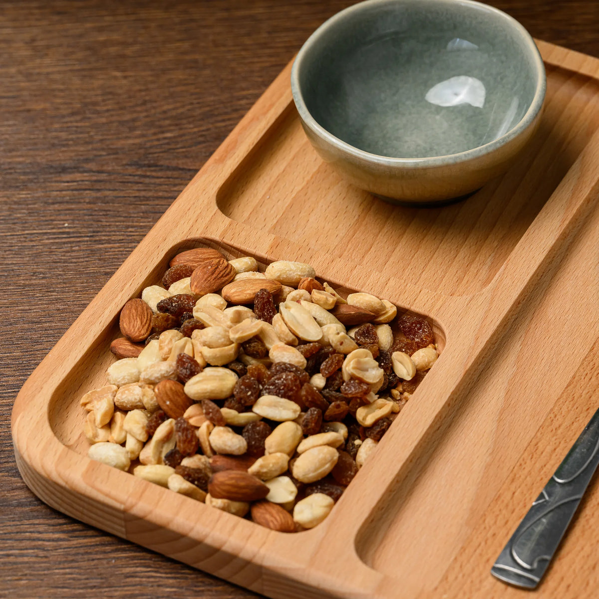 Ceramic bowl and mixed nuts filling two compartments of the beech wood serving board, knife visible at the edge