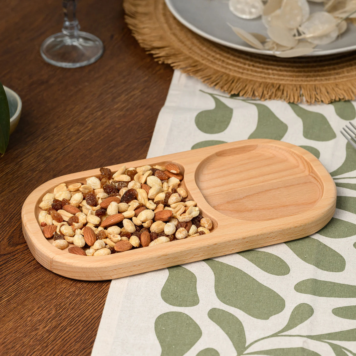 Beech wood serving board with two oval compartments, one holding mixed nuts, styled with a ceramic bowl