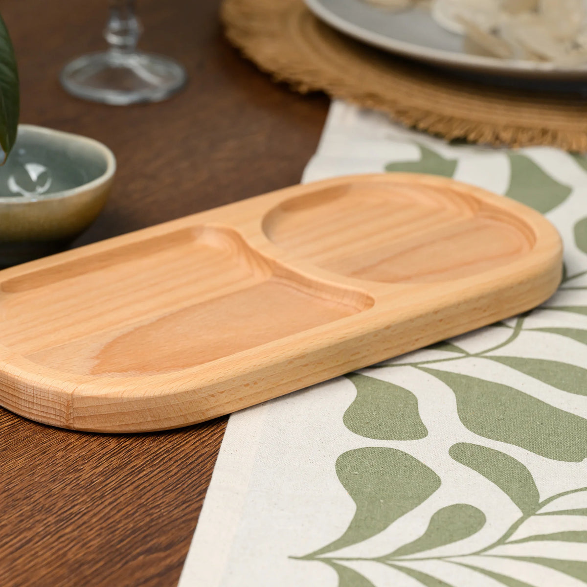 Angled view of the beech wood board with mixed nuts filling one oval compartment and the other left empty