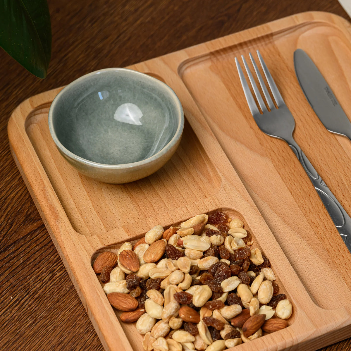 Overhead view of the beech wood serving board styled with a ceramic bowl, cutlery, and a mix of nuts and raisins