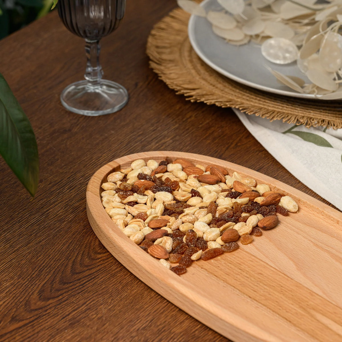 Close-up of mixed nuts and raisins filling half of the beech wood oval serving board, grain visible