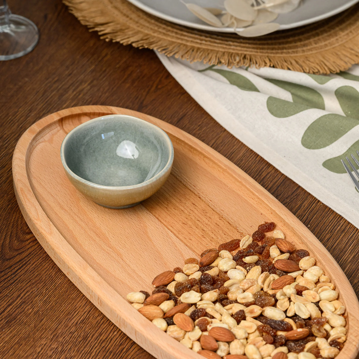 Ceramic bowl and a small pile of mixed nuts placed in the corner of the beech wood oval serving board