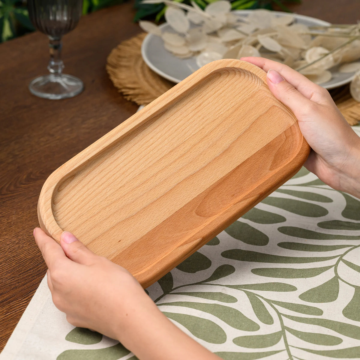 Hands holding the beech wood rectangular serving board at an angle above a table set with a wine glass